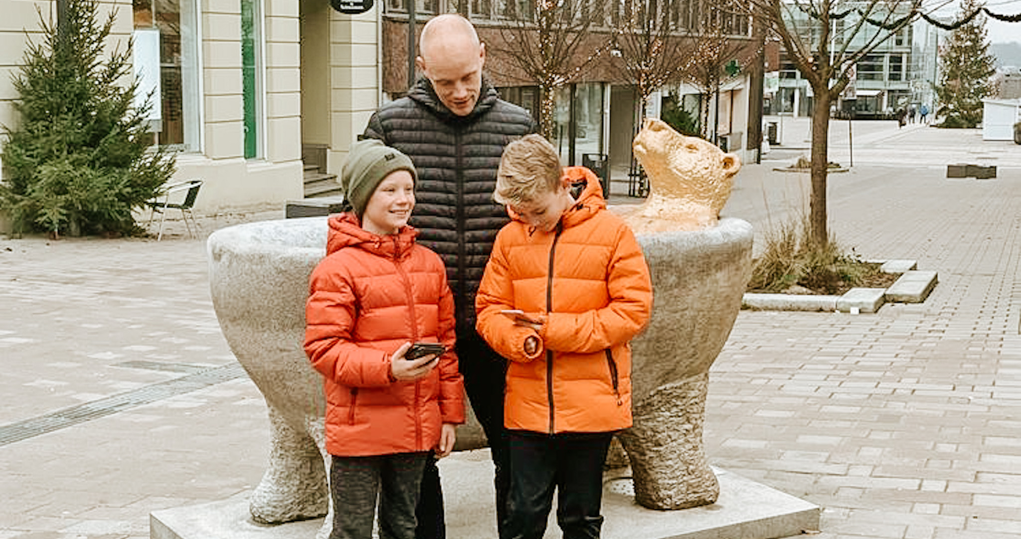 To gutter og en pappa spiller vandrespill på mobil i gågata i Sarpsborg. Foto.