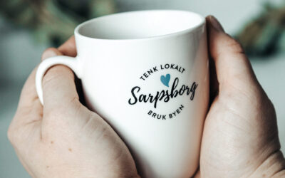 Hender som holder i en kaffekopp med påskriften: Sarpsborg, tenk lokalt, bruk byen. Foto.