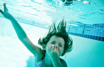 Jente som holder seg for nesen under vann i et basseng. Foto.