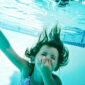 Jente som holder seg for nesen under vann i et basseng. Foto.